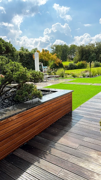 Jardin paysager contemporain extérieur, terrasse en lame de bois composite foncé, bordure en bois exotique teinté avec bassin décoratif en granit noir