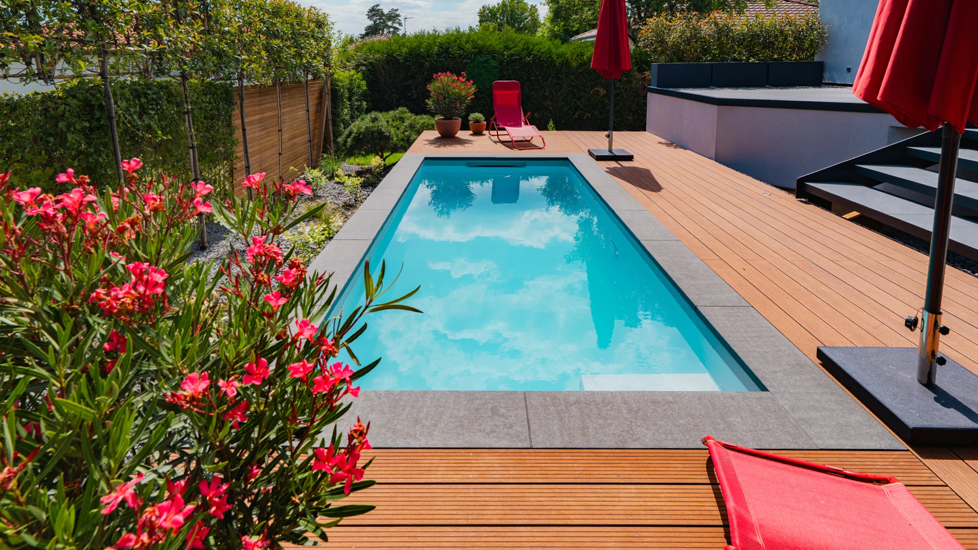 Jardin résidentiel moderne avec terrasse en bois composite brun foncé surélevée, intégrant un spa ou bassin en acier inoxydable