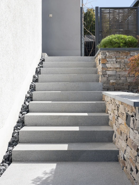 Terrasse extérieure moderne avec escalier en dalles de béton désactivé en porte-à-faux, accédant à une terrasse surélevée avec salon de jardin aluminium