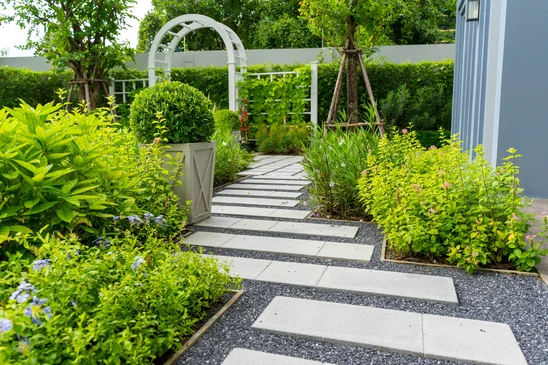 Chemin en pav&eacute;s de pierre naturelle grise traversant une pelouse verte luxuriante parsem&eacute;e de petites fleurs blanches et jaunes
