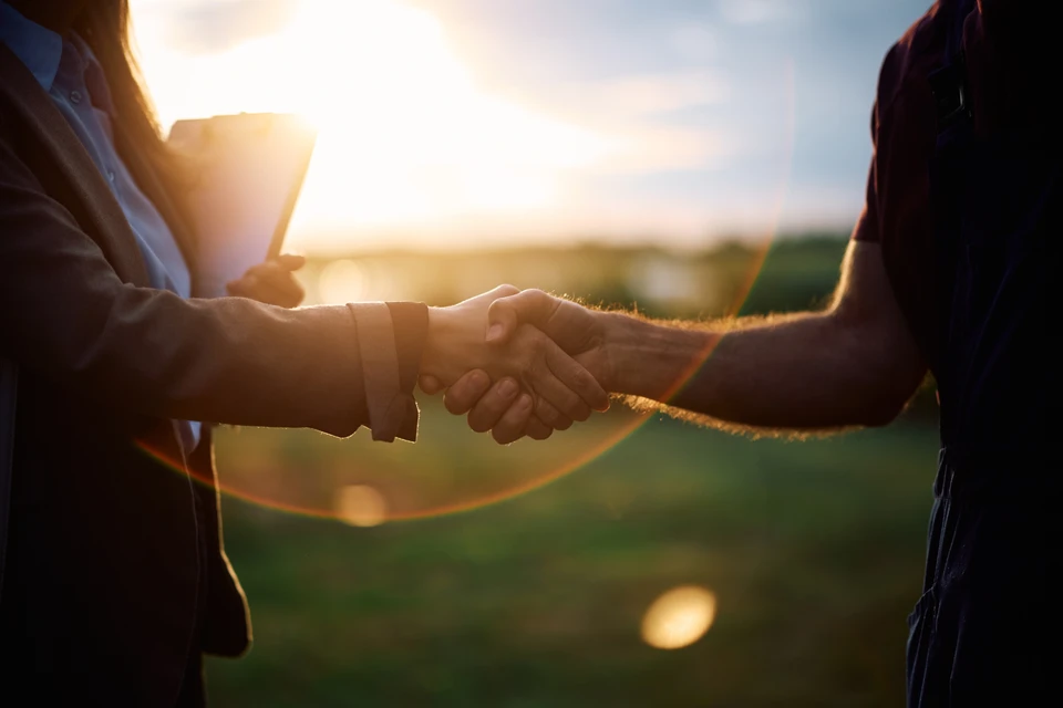 Photographie en plein jour montrant un professionnel en tenue de chantier (gilet de sécurité, chaussures de sécurité) conversant ou travaillant activement sur un chantier d'aménagement extérieur. Le contexte doit clairement montrer une interaction avec le client ou une activité de construction (pose de terrasse, pavage, clôture ou aménagement paysager visible en arrière-plan). L'image doit transmettre professionnalisme, engagement et implication sur le terrain.
