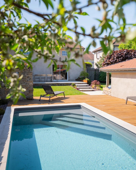 Piscine rectangulaire extérieure aux eaux turquoise, entourée d'une terrasse en bois composite IPE et d'un dallage en travertin beige