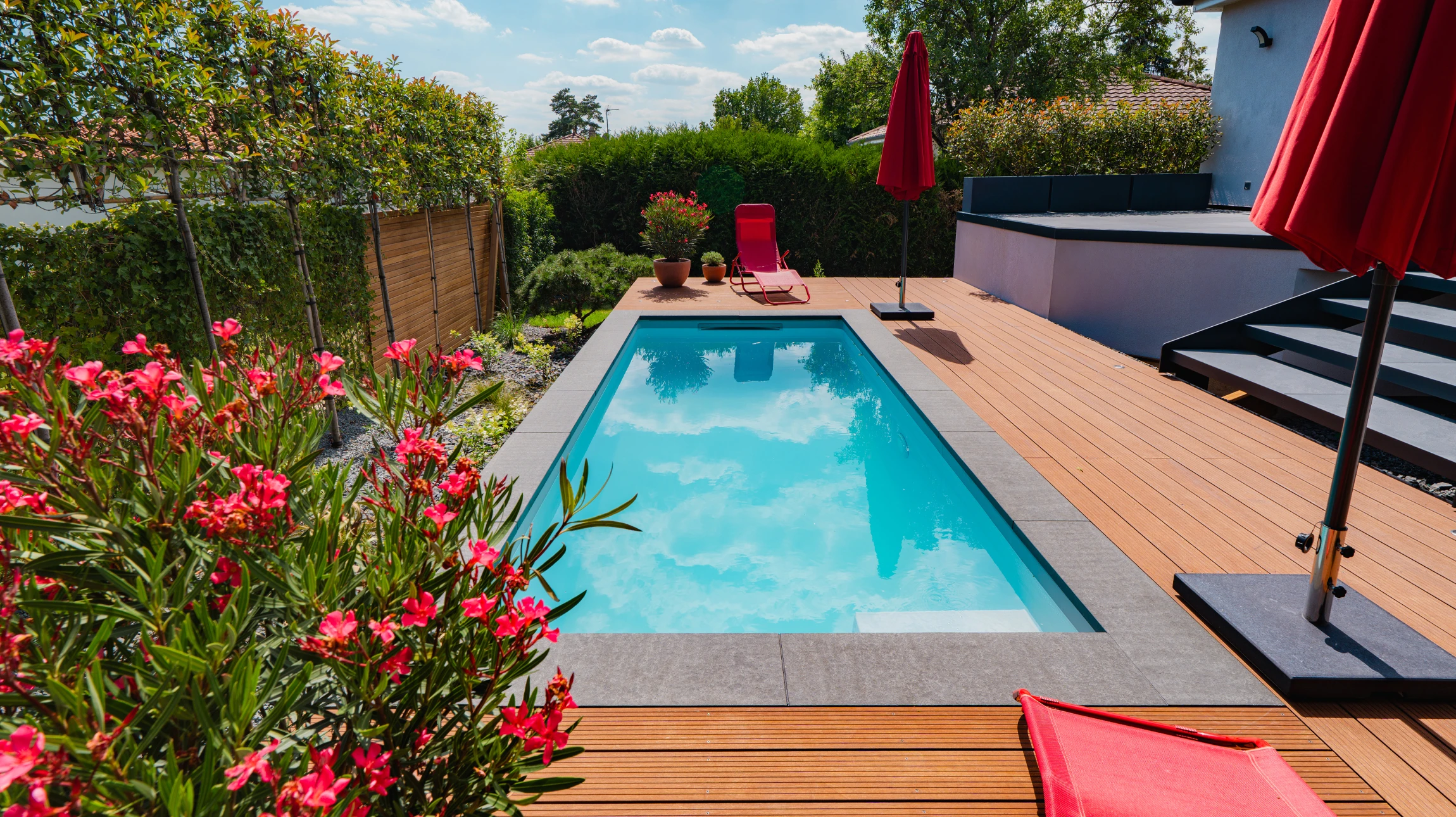 Espace extérieur résidentiel avec piscine rectangulaire moderne à débordement, terrasse en dalles contemporaines et margelles grises