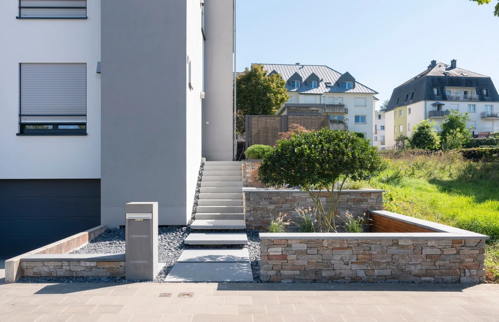 Allée d'entrée privée bordée d'arbres matures, portail ouvert avec piliers en pierre naturelle et ferronnerie noire