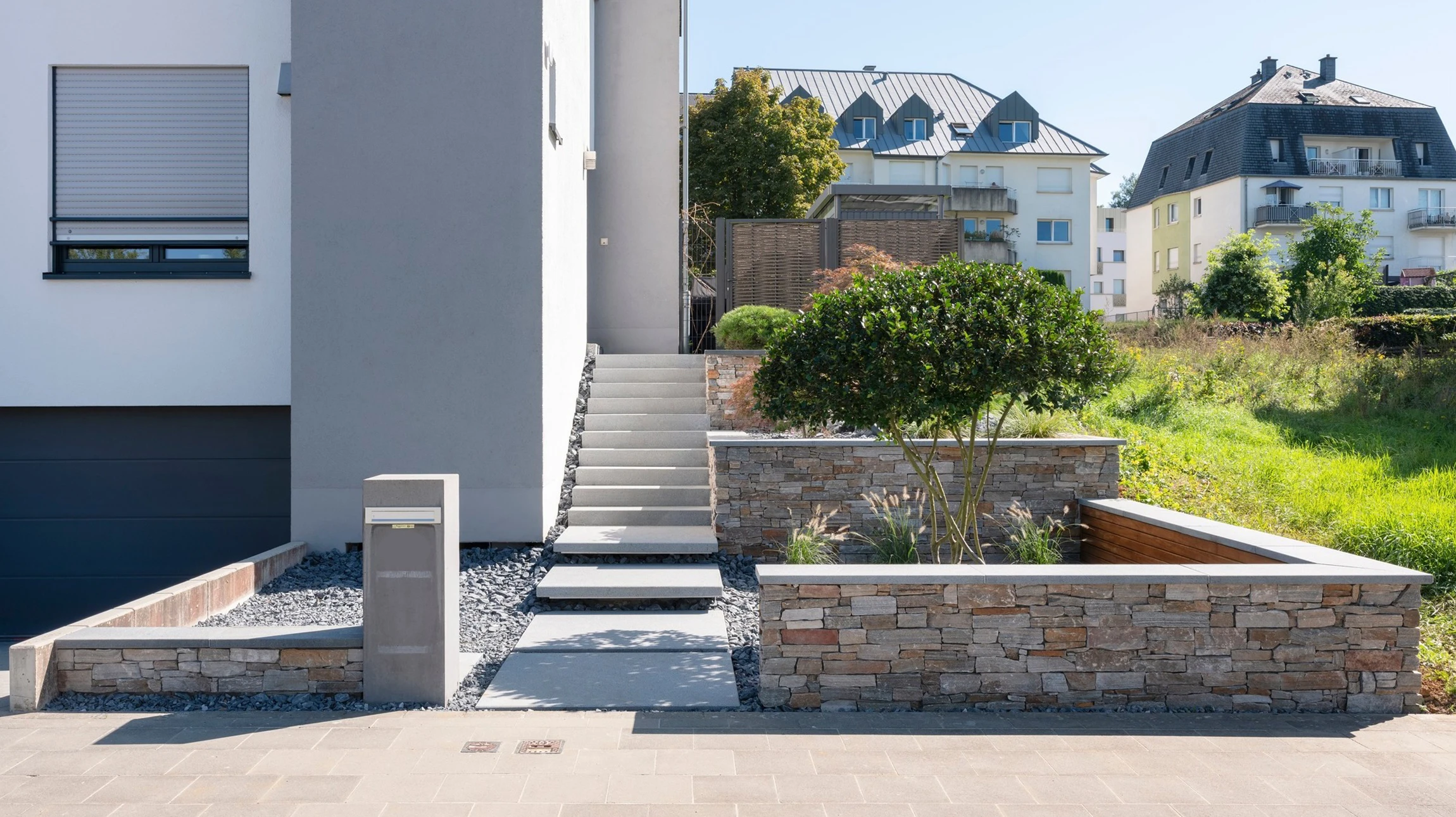 Escalier extérieur en pierre naturelle avec muret de soutènement, bordé de massifs de népéta en fleurs violettes
