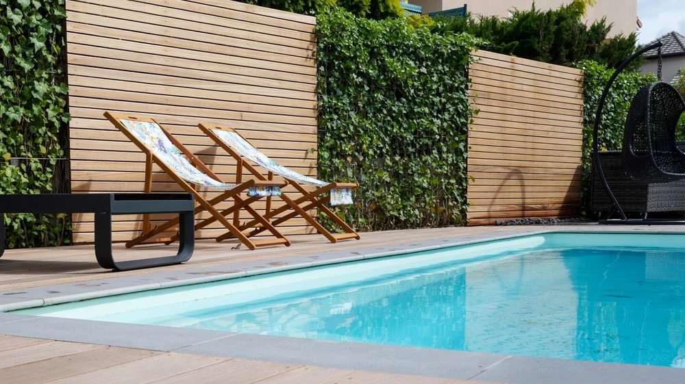 Photographie d'un jardin paysag&eacute; premium montrant un ensemble coh&eacute;rent d'am&eacute;nagements ext&eacute;rieurs&nbsp;: une terrasse pav&eacute;e en pierre naturelle au premier plan, une cl&ocirc;ture ou portail design en arri&egrave;re-plan, des plantations vari&eacute;es et bien int&eacute;gr&eacute;es (arbustes, massifs fleuris, conif&egrave;res), et des &eacute;l&eacute;ments de circulations am&eacute;nag&eacute;es (all&eacute;es), tous harmonieuement compos&eacute;s dans une mise en sc&egrave;ne globale d'am&eacute;nagement ext&eacute;rieur complet et de haut standing