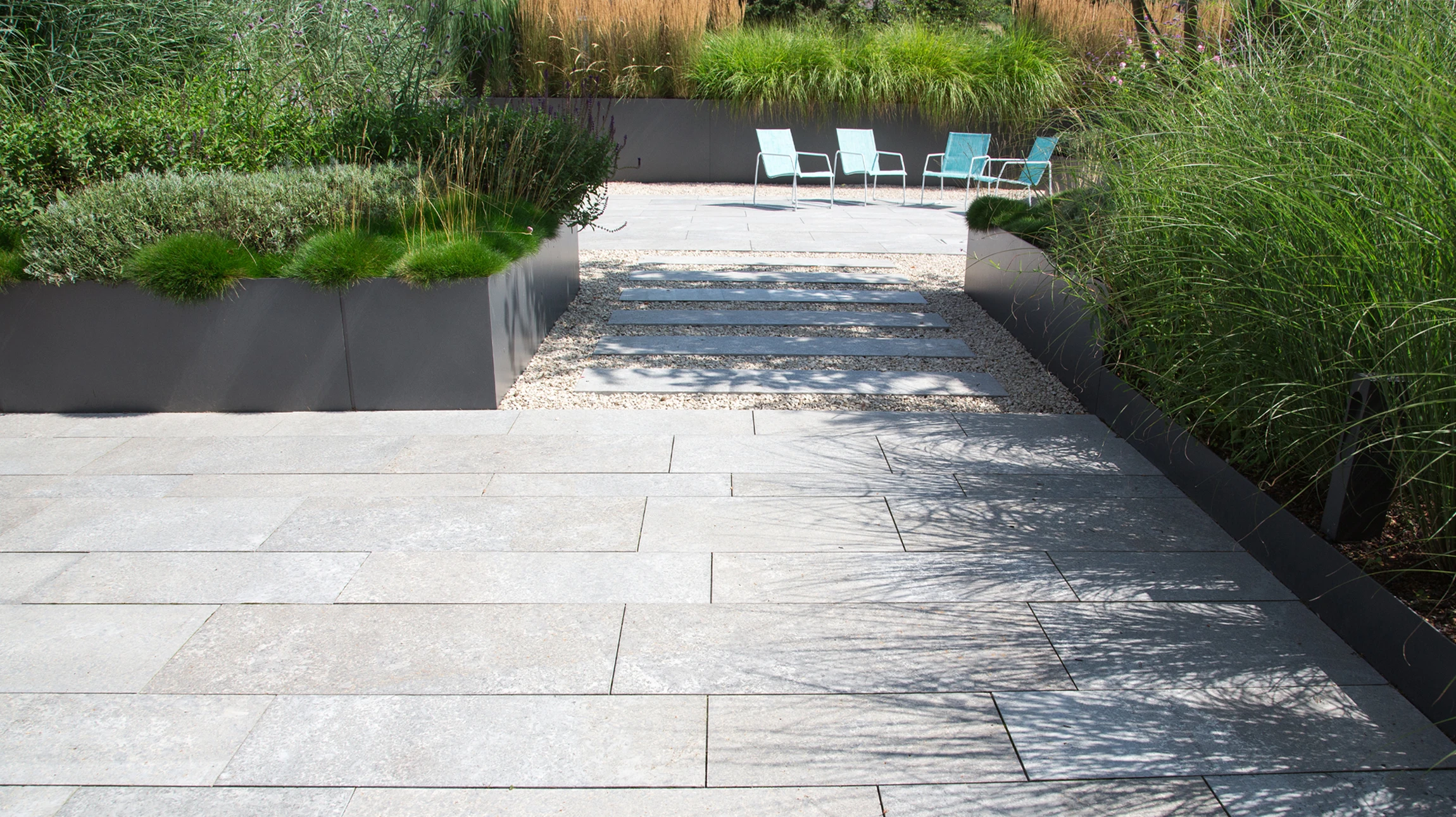 Jardin paysager extérieur avec allée courbe en dalles de grès rose disposées en quinconce sur pelouse verte entretenue